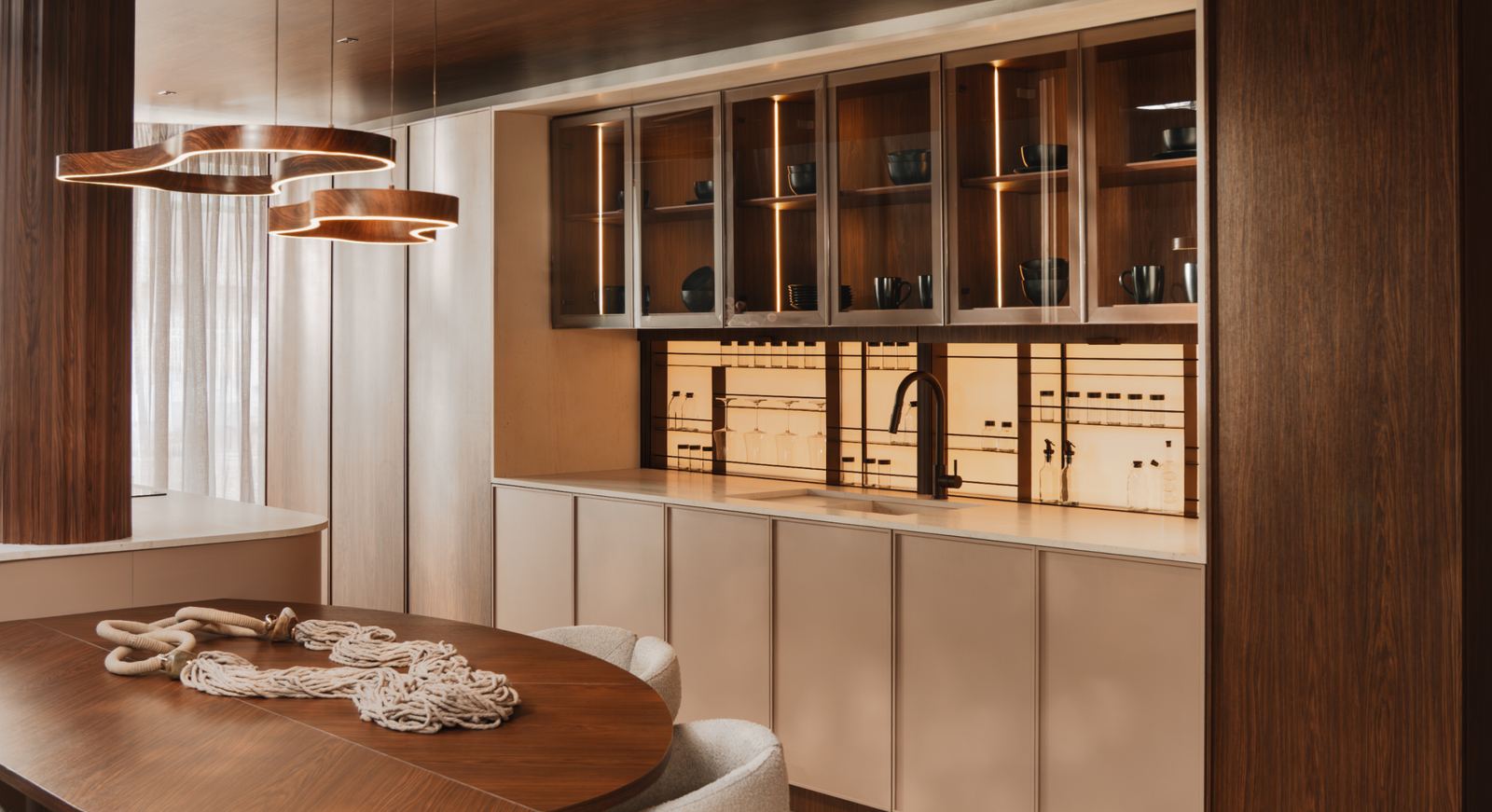 Sala de jantar integrada à cozinha, com mesa oval de madeira, luminárias circulares e marcenaria em Carvalho Aurum e Mocca.
