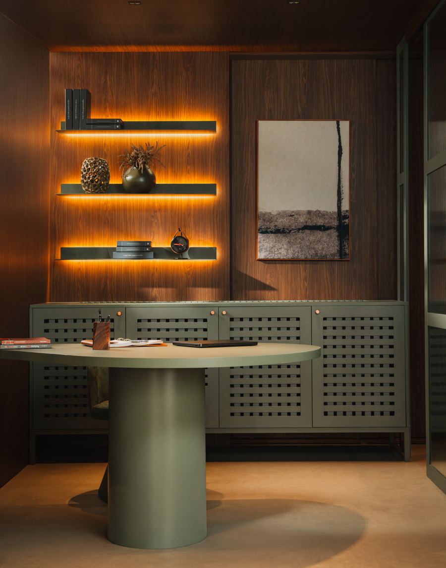 Home office com armários em Foglio de portas Muxarabi, prateleira iluminada e mesa redonda com base cilíndrica verde.