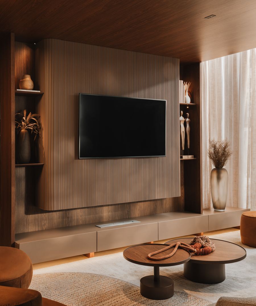 Sala de estar com painel ripado em Carvalho Aurum, televisor embutido, mesas de centro redondas e poltronas em tom terroso.